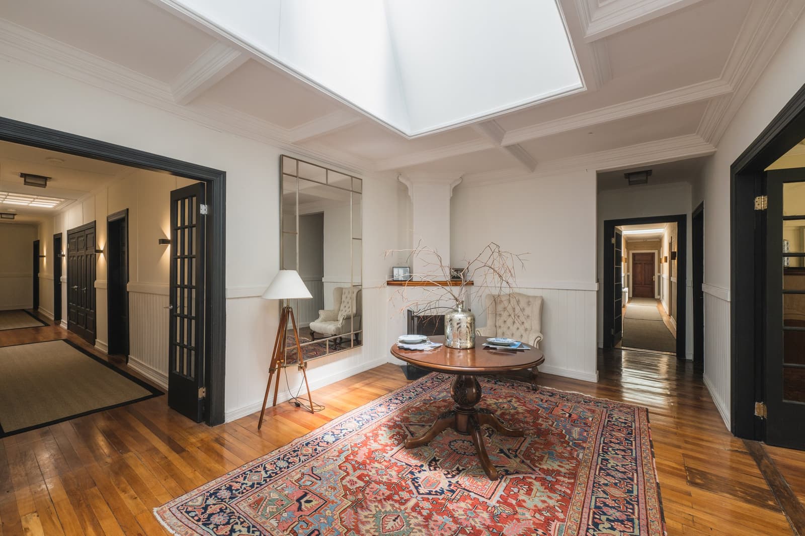 Old bones, good light, and a rug that has seen a few wool seasons. Photo: CARLOS DIAZ Sun-lit entrance hall of estancia cerro guido featuring a large skylight, polished hardwood floors, a round pedestal table on a red Persian rug, a tufted wingback chair, and dark-framed French doors opening to corridors on either side