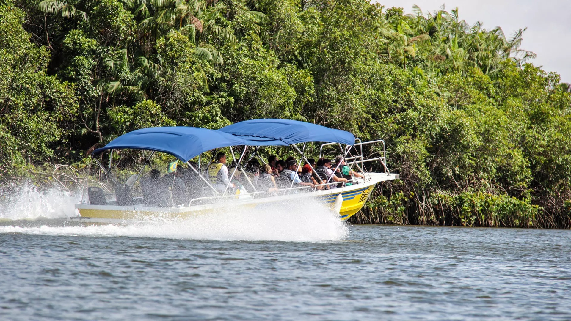 Passagiere fahren in einem gelben Motorboot mit blauen Verdecken auf dem Rio Preguiças in Richtung Atins.