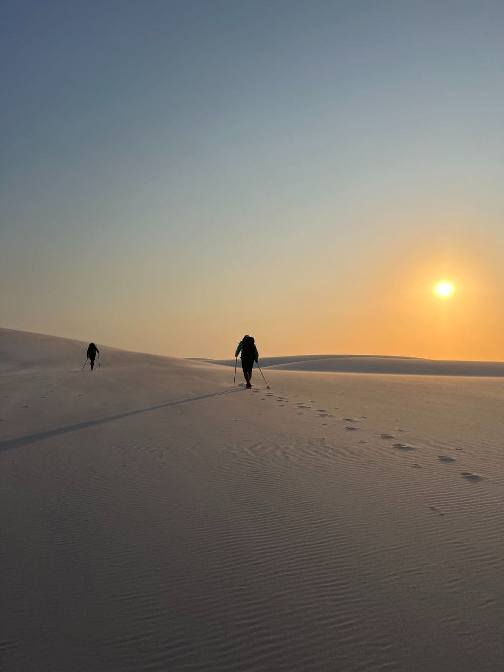 Die Silhouetten von Menschen spazieren bei Sonnenuntergang über die Sanddünen der Lençóis Maranhenses.