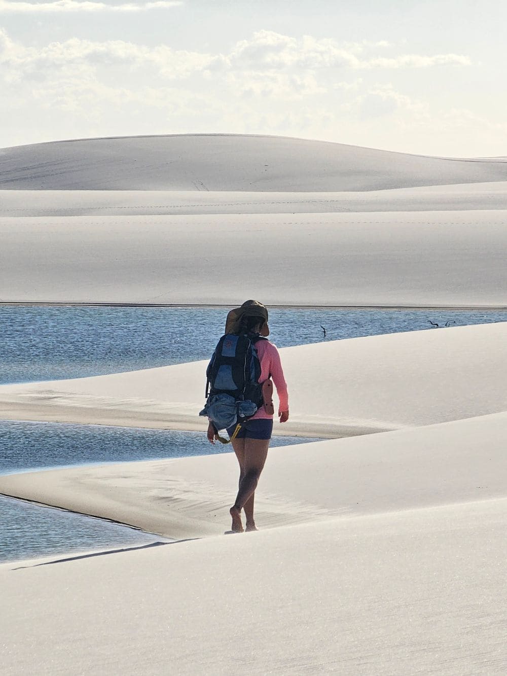 Ein Reisender mit Rucksack geht barfuß am Ufer einer friedlichen Lagune in Santo Amaro spazieren.