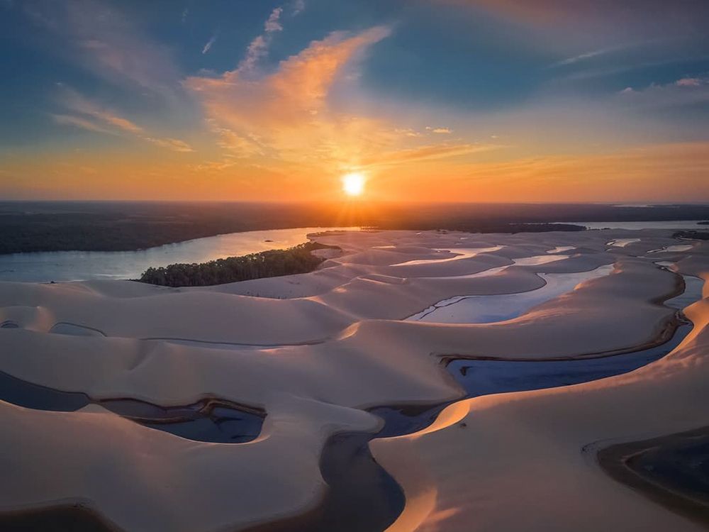 Vue aérienne des dunes du Brésil avec des chenaux d’eau sinueux reflétant la lumière dorée d’un coucher de soleil éclatant.