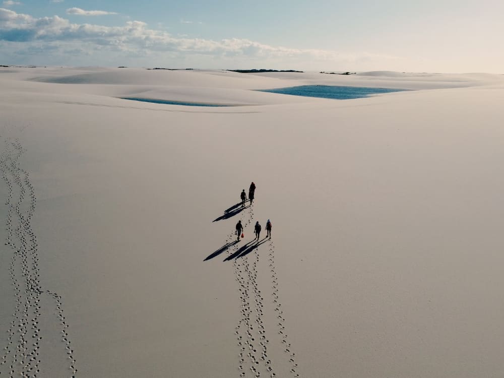  Eine Gruppe von Menschen wirft lange Schatten bei der Erkundung der Sanddünen in der primitiven Zone der Lençóis Maranhenses.