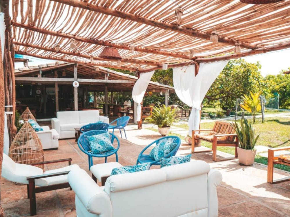 Rustikaler sozialer Außenbereich einer Pousada, überdacht von einer unregelmäßigen Holzkonstruktion und ausgestattet mit bequemen weißen Sofas und blauen Stühlen.