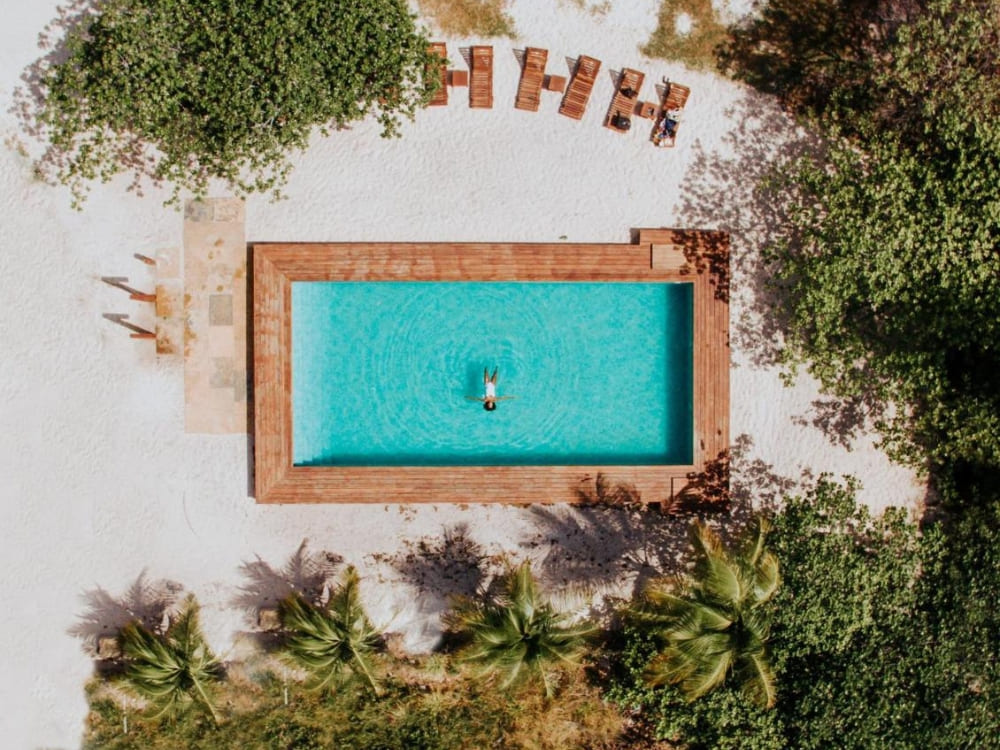 Vertikale Luftaufnahme eines rechteckigen, türkisfarbenen Swimmingpools mit glattem Holzdeck und Liegestühlen im luxuriösen La Ferme De Georges.