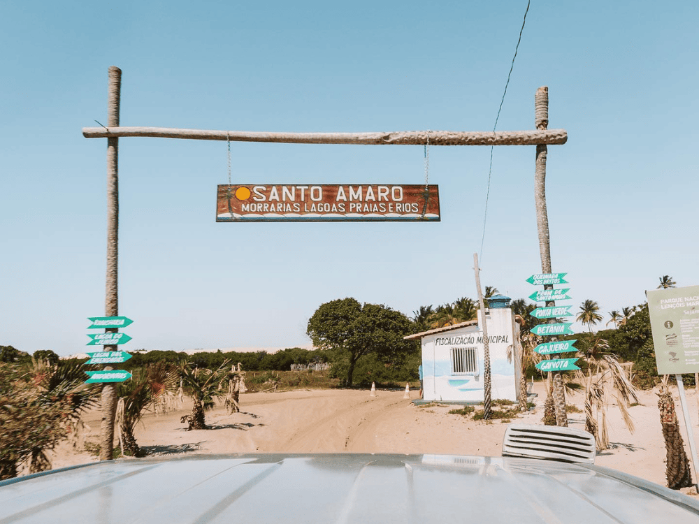 Rustikaler Portikus mit einem Holzschild, das den Text "Santo Amaro Morvanas Lagoas Prajasthios" über einem Sandweg anzeigt.