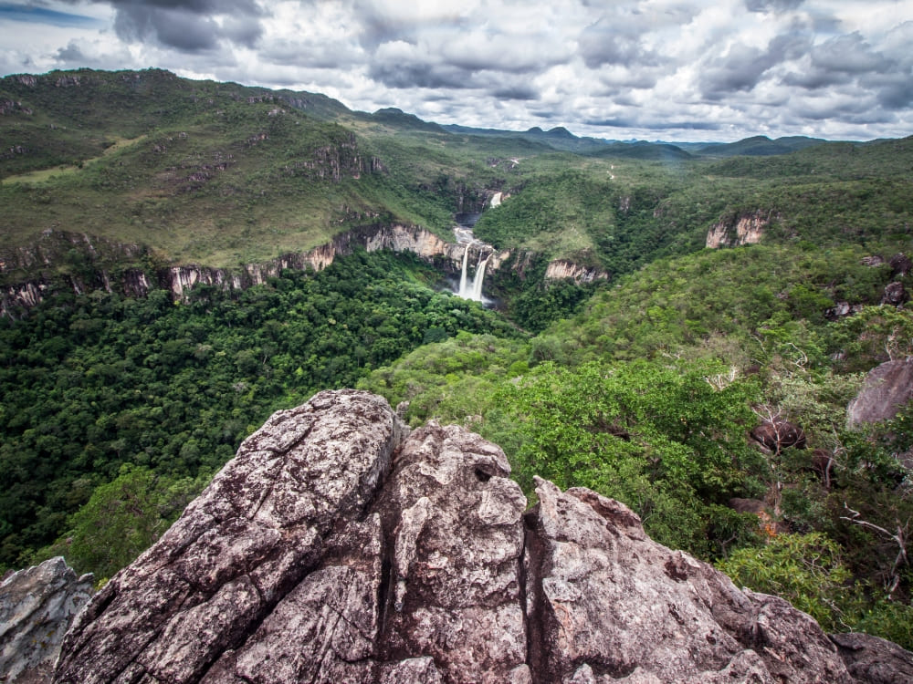 Vue depuis un promontoire rocheux montrant une cascade au loin et une végétation luxuriante dans le parc national de Chapada dos Veadeiros.