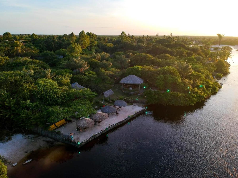 Luftaufnahme des im Camp-Stil gehaltenen Ciamat Camps, mit strohgedeckten Kiosken und einem von Vegetation umgebenen Holzdeck am Wasser.