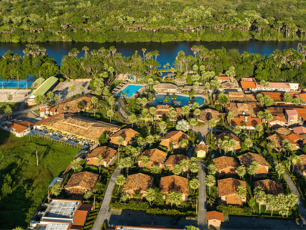 Luftaufnahme der großen Swimmingpools und der Chalet-Infrastruktur mit Ziegeldächern im Porto Preguiças Resort, direkt am Fluss gelegen.