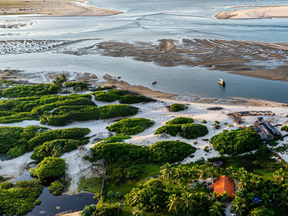 Üppige Luftlandschaft von Atins, die die grüne Vegetation, die Sandbänke und das Zusammentreffen des Preguiças-Flusses mit dem Ozean hervorhebt.