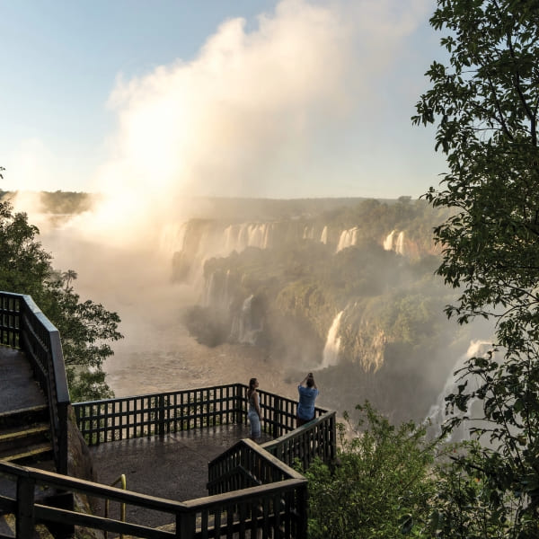 Toeristen observeren de enorme Iguacu-watervallen vanaf een houten uitkijkplatform gehuld in mist.
