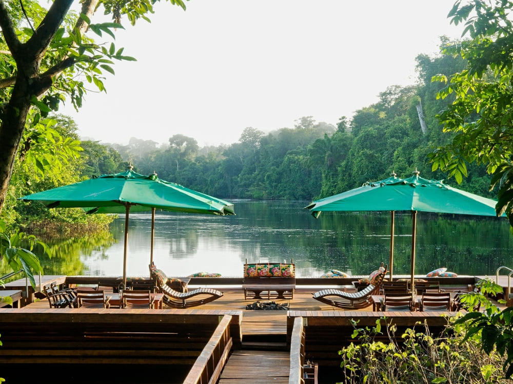 Houten terras met groene parasols en ligstoelen met uitzicht op een serene Amazonerivier.
