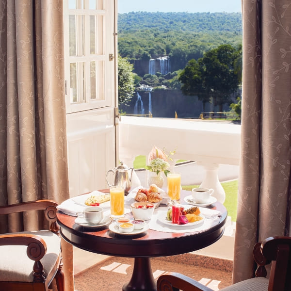 Ontbijttafel gedekt voor twee op een balkon met uitzicht op de kletterende Iguacu-watervallen.