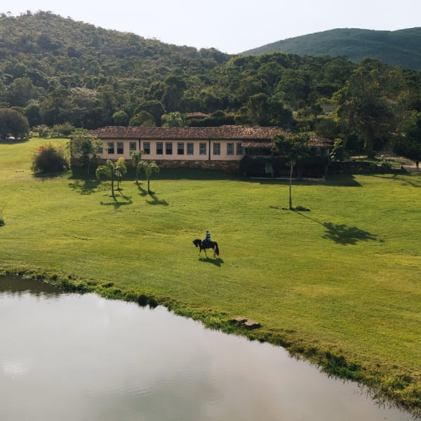 Persoon te paard over een uitgestrekt groen grasveld naast een meer op het platteland van Minas Gerais.