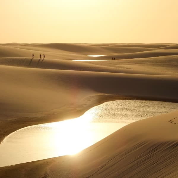 Mensen wandelen over uitgestrekte witte zandduinen bij kristalheldere lagunes bij zonsondergang.