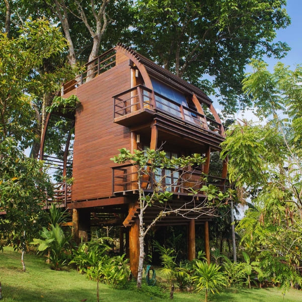 Houten boomhutbungalow met meerdere verdiepingen, omringd door weelderig groen bij een luxe ecolodge in de Amazone.