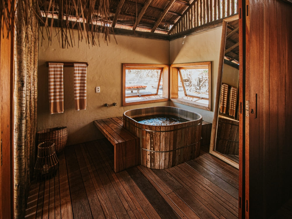 Houten badkuip naast grote ramen in een rustieke suite bij Pousada Trijuncao.