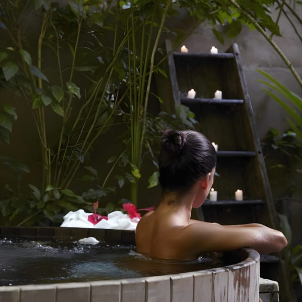Vrouw ontspant 's nachts in een ronde houten buitenjacuzzi omringd door tropische planten.