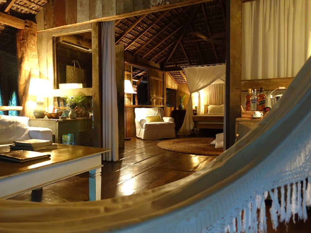 Uitzicht vanuit een hangmat kijkend in een warm verlichte rustieke suite met houten vloeren bij UXUA.