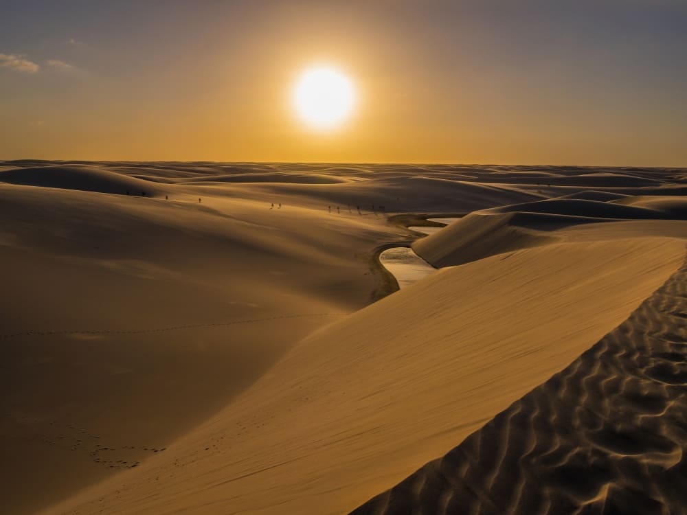 Le soleil se couche sur des dunes de sable ondulantes et un cours d’eau peu profond serpentant à travers le Parc national des Lençóis Maranhenses au Brésil.