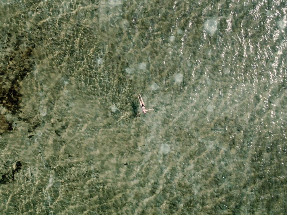 Vue du dessus d’une personne nageant dans une eau peu profonde et cristalline au fond sablonneux texturé lors d’une excursion dans le parc national des Lençóis Maranhenses.