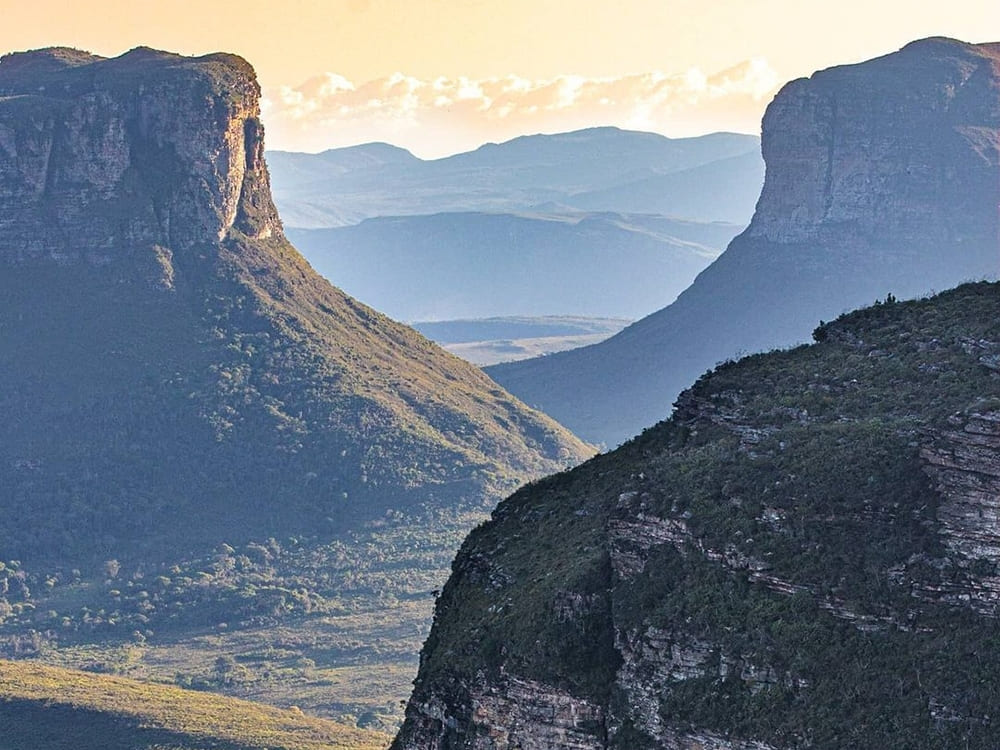 Two massive, flat-topped mountains rise on either side of a deep, lush green valley under a soft sunset sky.