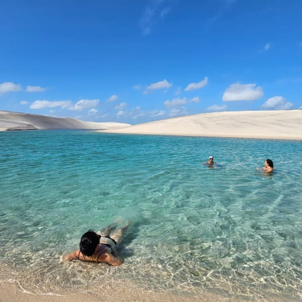 Des touristes se détendent dans les eaux peu profondes et cristallines d'une lagune entourée de dunes de sable blanc aux Lençóis Maranhenses.